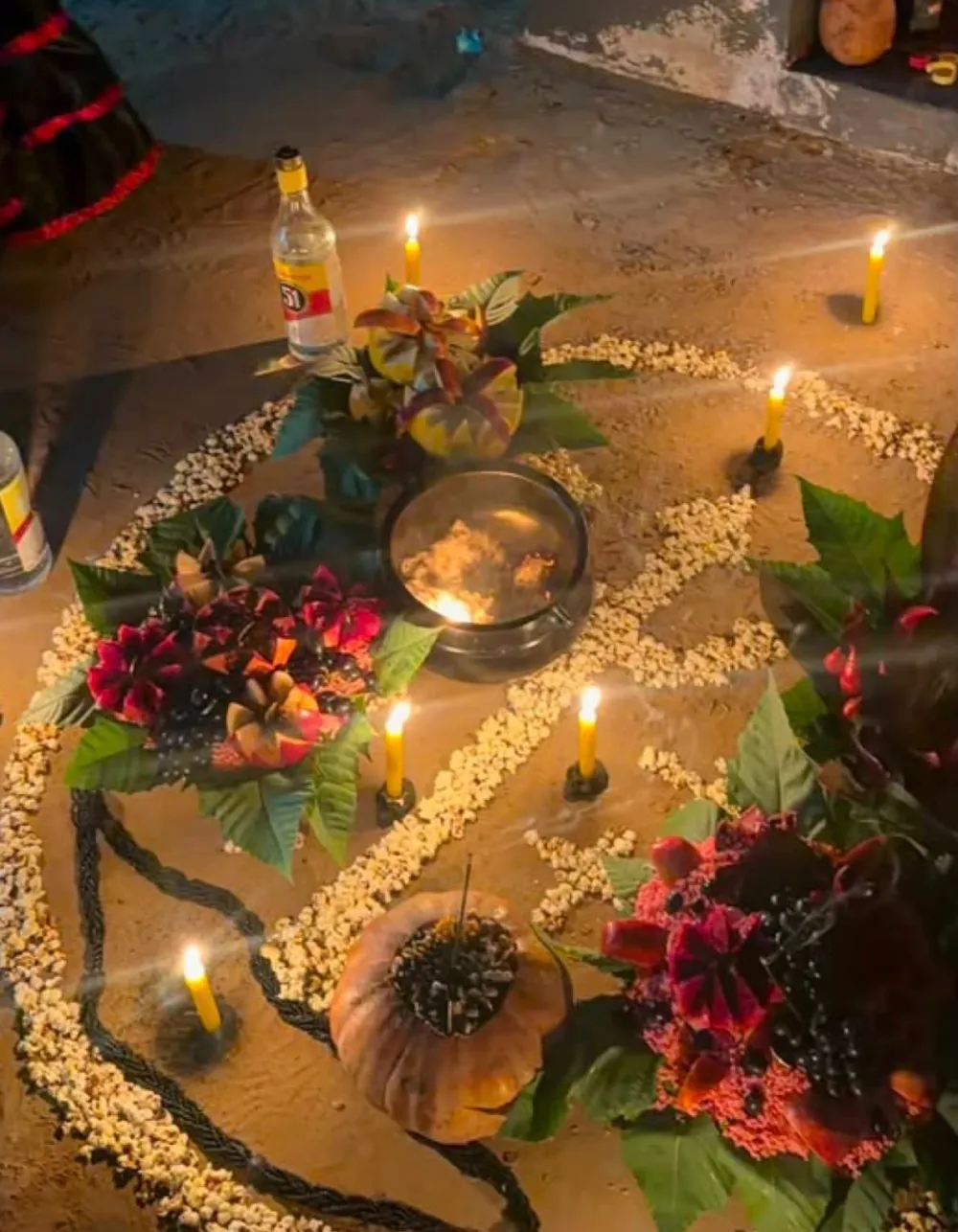 Ritual no chão com velas amarelas, pipoca em círculo, flores escuras e abóbora com incenso